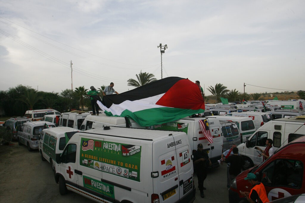 International peace activist hold Palestinian flag as their aid convoy wait to cross in to Gaza at the Rafah border Crossing between Egypt and the Gaza Strip, Thursday, Oct. 21, 2010. The aid convoy arrived in the Gaza Strip overland from Egypt on Thursday to a warm welcome from the territory's Islamic militant, The convoy was organized by 'Viva Palestina,' headed by former British member of parliament George Galloway. Egypt banned Galloway from accompanying the convoy because of previous clashes with Egyptian security. Hamas official Ahmed Youssef said the aid is worth about $5 million and includes 137 used vehicles for ambulances and transport.(AP Photo/Eyad Baba)